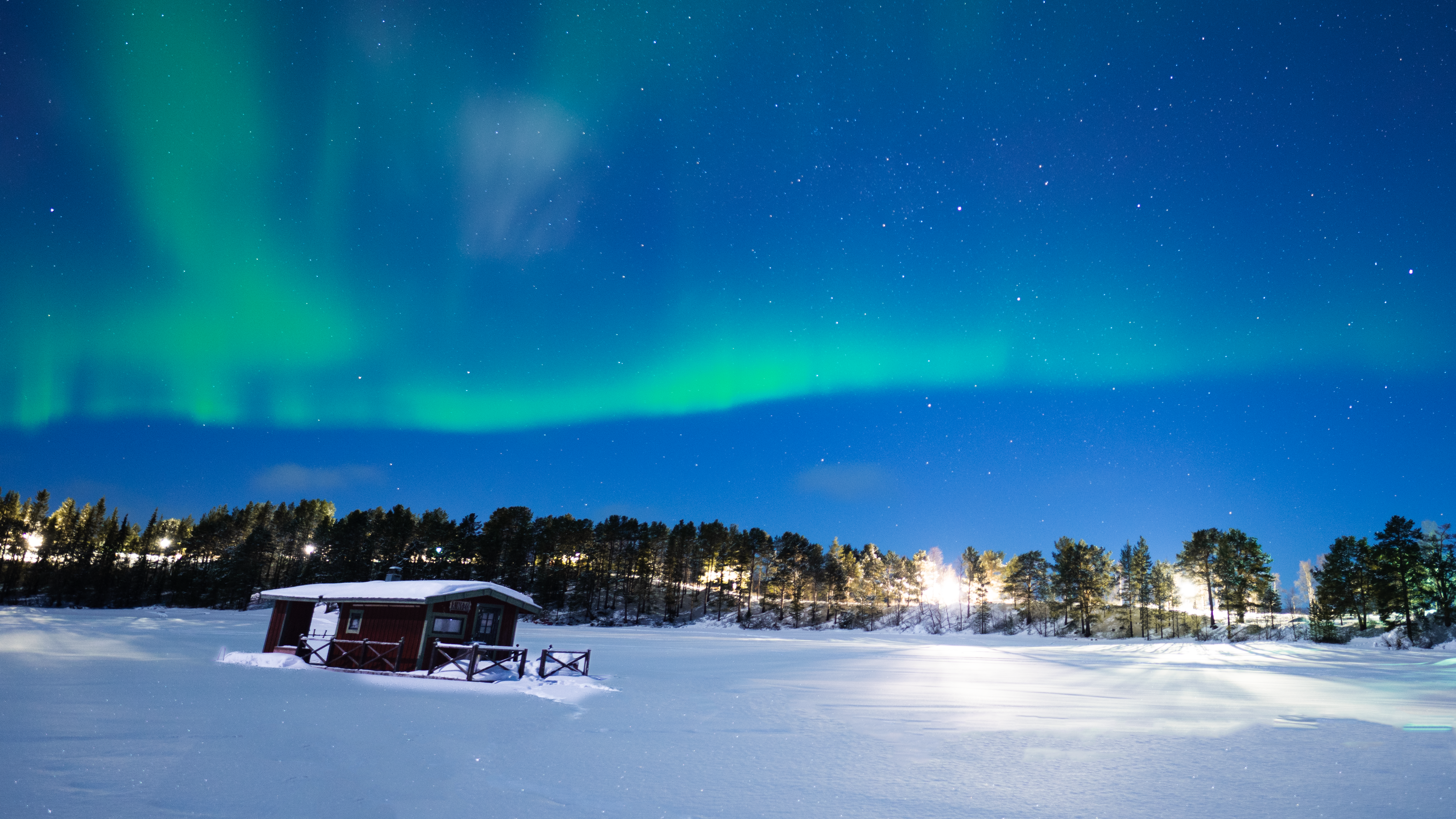 Northern Lights with snow on the ground and red hut in foreground